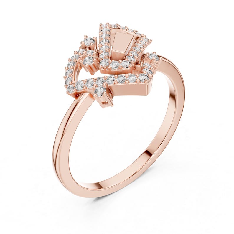 May include: Rose gold ring featuring a geometric design encrusted with small, sparkling clear stones. The ring's band is a smooth, polished rose gold, and the setting is a cluster of stones. The ring is set against a white background.
