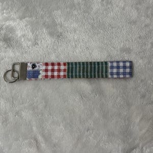 May include: A fabric keychain with a silver metal ring. The keychain is made of four sections of patterned fabric: a blue floral print, red and white gingham, green stripes, and blue and white gingham.