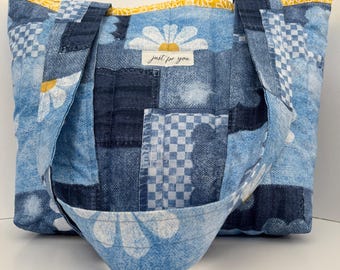 Könnte beinhalten: Eine Denim-Tragetasche mit Patchwork-Design. Die Tasche hat eine Gänseblümchen-Applikation und den Text "just for you" auf einem weißen Etikett. Das Innenfutter ist gelb mit einem Gänseblümchenmuster, und die Griffe sind aus dem gleichen Denim-Material.