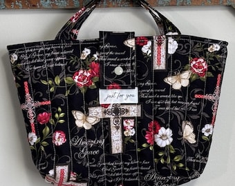 Könnte beinhalten: Schwarze, gesteppte Tragetasche mit Blumen- und Kreuzmuster. Mit roten und weißen Blumen, Schmetterlingen und den Worten "Amazing Grace" und "just for you". Enthält zwei schwarze Griffe.