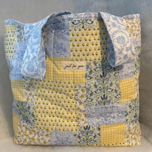May include: A patchwork tote bag with blue and yellow floral and gingham patterns. The bag features a rectangular shape with two handles and the text "just for you" on a small label.
