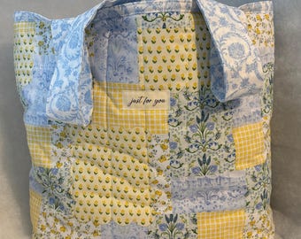 Könnte beinhalten: Eine Patchwork-Tragetasche mit blau-gelben Blumen- und Vichy-Mustern. Die Tasche hat zwei Henkel und den Text "just for you" auf einem kleinen Etikett. Die Tasche ist aus gestepptem Stoff gefertigt.