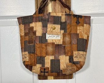 Könnte beinhalten: Eine gesteppte Stofftasche mit Patchwork-Design in Braun- und Beigetönen. Der Stoff ist mit religiösen Kreuzen und inspirierenden Texten wie "Praise", "Be Strong" und "Great Strength" bedruckt. Sie verfügt über einen Druckknopfverschluss.