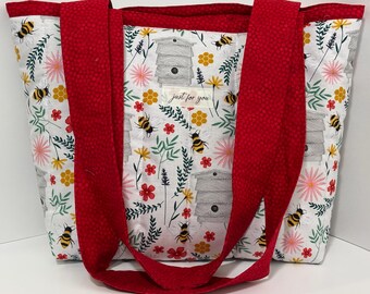 Könnte beinhalten: Eine weiße Tragetasche mit Blumen- und Bienenmuster. Die Tasche hat rote Griffe und Verzierungen. Das Design umfasst Bienen, Bienenstöcke und Blumen. Der Text "just for you" ist auf der Vorderseite der Tasche zu sehen.