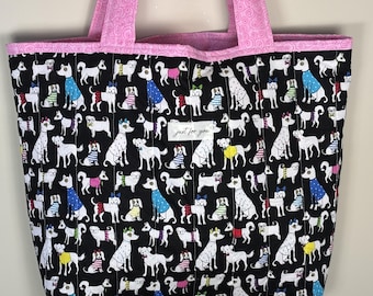 Könnte beinhalten: Gesteppte Tragetasche mit schwarzem Hintergrund, bedeckt mit weißen Hundeillustrationen in bunten Pullovern. Die Tasche hat rosa Griffe und eine rosa Innenverkleidung. Der Text "just for you" ist auf der Vorderseite.