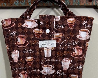 Könnte beinhalten: Braune, gesteppte Tragetasche mit Kaffeemuster. Die Tasche zeigt verschiedene Kaffeetassen-Illustrationen und kaffeebezogene Wörter wie "Caffe", "Latte" und "Mocha". Sie hat einen Knopfverschluss und ein kleines Etikett mit der Aufschrift "just for you".