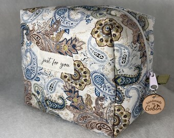 Könnte beinhalten: Eine quadratische Kosmetiktasche mit einem Paisley-Muster in Blau-, Braun- und Beigetönen. Die Tasche hat einen Reißverschluss und ein kleines Holzschild mit der Aufschrift "handmade by Gobin". Der Text "just for you" steht auf der Vorderseite.