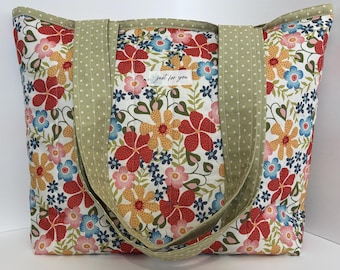 Könnte beinhalten: Eine florale Tragetasche mit einem Muster aus roten, gelben, blauen und rosa Blumen auf weißem Hintergrund. Die Tasche hat olivgrüne Griffe und Verzierungen mit weißen Punkten. Der Text "just for you" ist sichtbar.