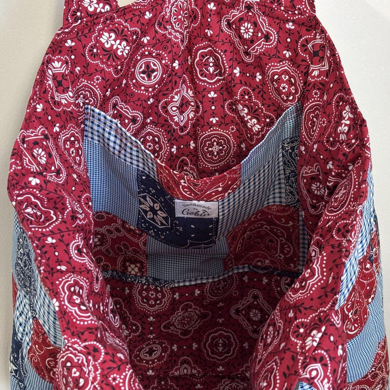 May include: A handmade tote bag with a red paisley pattern and white details. The interior has a blue and white gingham pocket and a blue and white paisley pocket. The label reads "Handmade by Gobis".