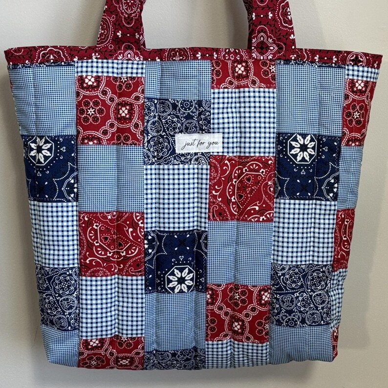 May include: A patchwork tote bag featuring red paisley, blue gingham, and navy floral patterns. The bag has sturdy handles and a label that reads "just for you". The bag is quilted and rectangular in shape.