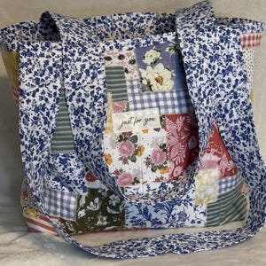 May include: A patchwork tote bag with a variety of floral and patterned fabrics in shades of blue, pink, red, and yellow. The bag features a blue floral print lining and straps, with the text "just for you" on a patch.