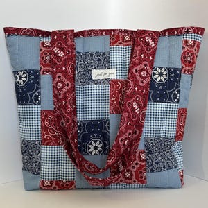 May include: A large patchwork tote bag with a mix of red paisley, navy blue floral, and light blue gingham fabrics. The bag has two handles and a tag that reads "just for you".