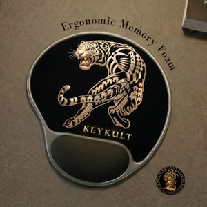 May include: Black ergonomic memory foam mousepad featuring a gold tiger design. The mousepad has a wrist rest and the text "KEYKULT" is printed on the bottom. The mousepad is designed for comfort and support for computer users.