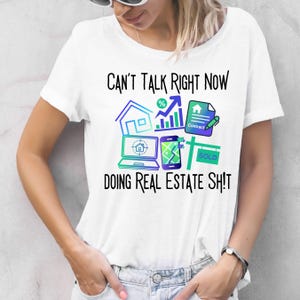 以下が含まれることがあります： 「CAN'T TALK RIGHT NOW DOING REAL ESTATE SH!T」の文字が入った白いTシャツ。家、ラップトップ、スマートフォン、契約書、そして「SOLD」のサインが青と緑の色合いで描かれています。