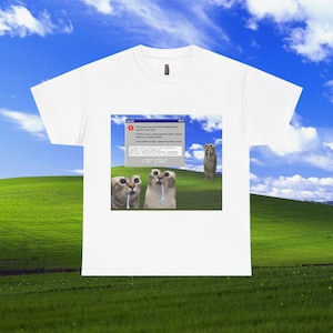 以下が含まれることがあります： CAT.EXEというタイトルのWindows風エラーメッセージボックスのグラフィックプリントが施された白い半袖Tシャツ。背景には緑の丘の風景が描かれ、3匹の猫がそれぞれ小さな白いスプーンを口にくわえている様子がプリントされています。