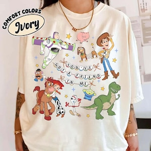 May include: Ivory-coloured t-shirt with a graphic of animated film characters. The design includes Buzz Lightyear, Woody, and other characters, with the phrase "YOU'VE GOT A FRIEND IN ME".