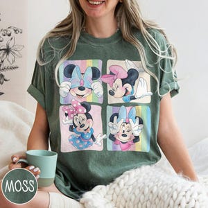 May include: Green t-shirt featuring four squares with Minnie Mouse illustrations. Each square showcases a different pose with colorful bows and backgrounds. The shirt is a relaxed fit, perfect for casual wear.