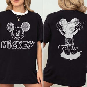 May include: Black t-shirt with a white Mickey Mouse design on the front and back. The front displays Mickey's face and the word "Mickey". The back shows Mickey with his arms raised in a peace sign.