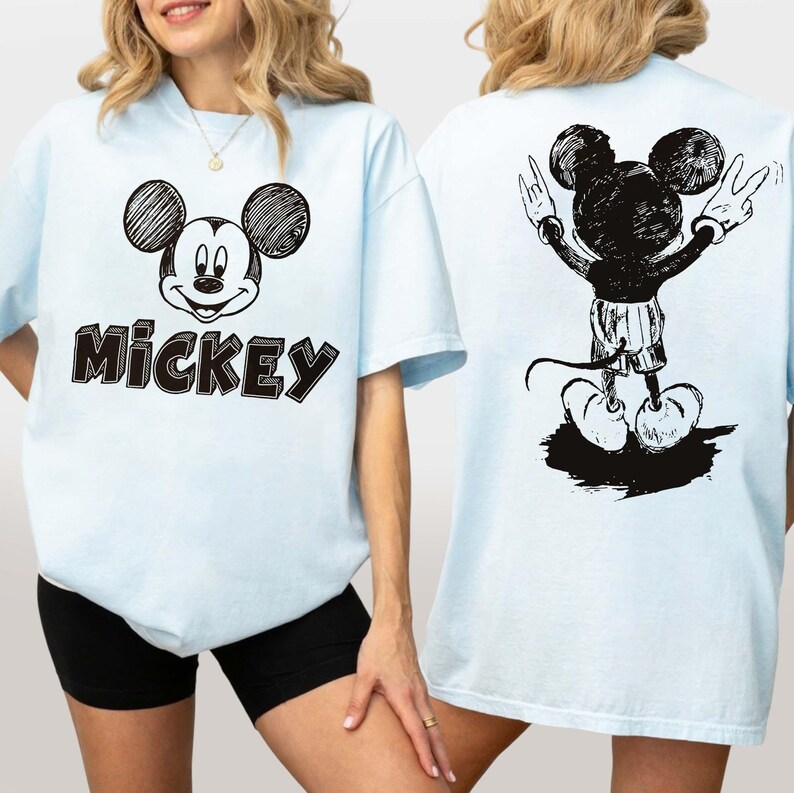 May include: Pale blue t-shirt with a black and white sketch of Mickey Mouse on the front and the word "Mickey" below. The back of the shirt features a larger sketch of Mickey Mouse with his arms raised in a peace sign.