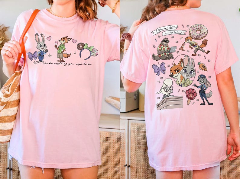 Puede incluir: Camiseta rosa claro con personajes de Zootopia. La parte delantera muestra a Judy Hopps, Nick Wilde y elementos tem&aacute;ticos de Disney con el texto "You can be anything you wish to be." La parte trasera presenta m&aacute;s personajes y texto.