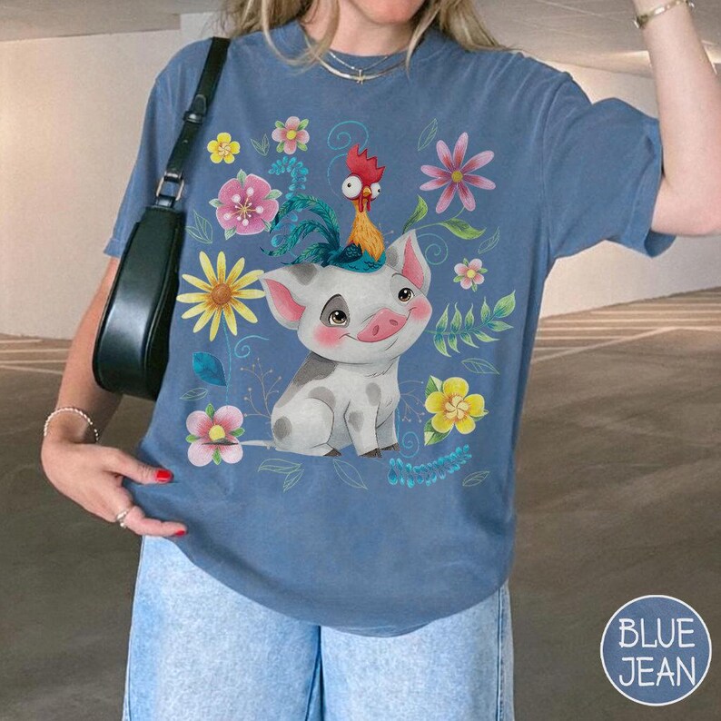 Pu&ograve; includere: T-shirt blu con un design a fumetto di maiale e gallo, circondato da fiori colorati. Il maiale &egrave; bianco con macchie grigie e un volto sorridente. Il gallo &egrave; giallo e rosso. La maglietta ha una vestibilit&agrave; ampia.