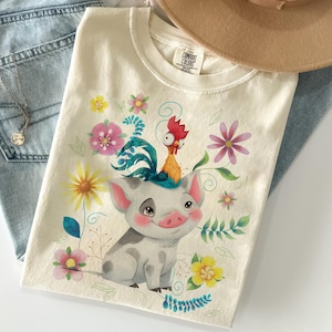 Pu&ograve; includere: T-shirt color crema con un maiale dei cartoni animati con un gallo in testa, circondato da fiori e foglie colorate. La maglietta &egrave; realizzata in un materiale morbido e fa parte di una collezione di abbigliamento.