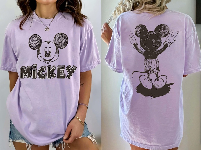 May include: A lilac t-shirt with a sketch of Mickey Mouse on the front and back. The front of the shirt has the word "Mickey" in a block letter style. The back of the shirt shows Mickey Mouse with his arms up in a peace sign.