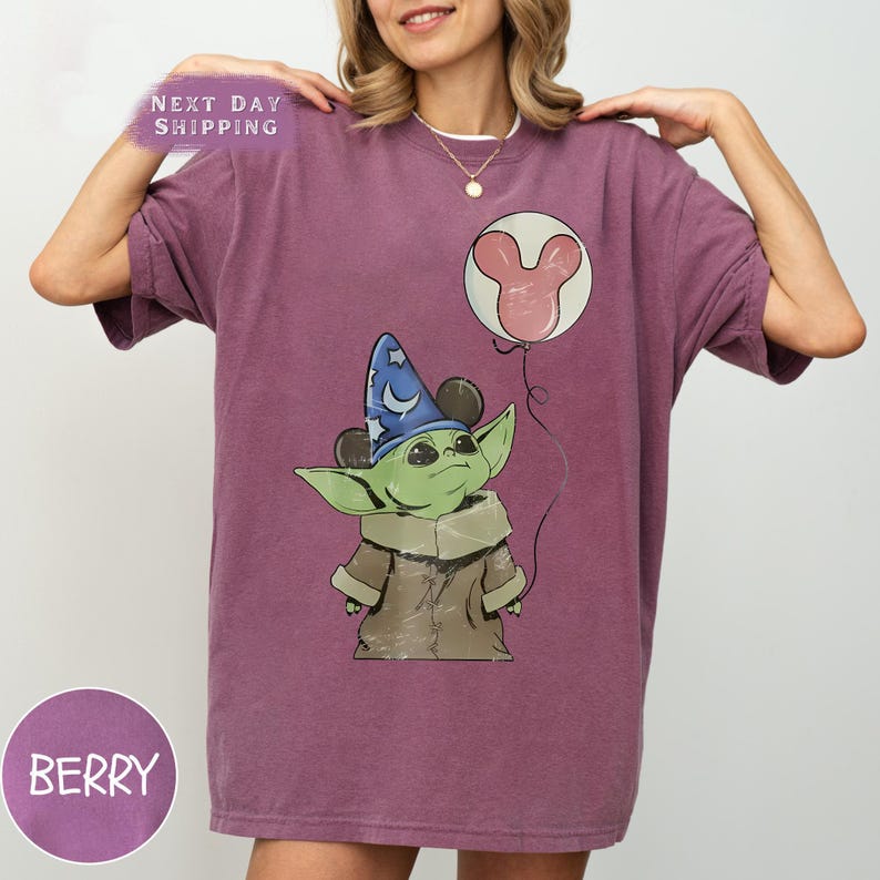 Puede incluir: Camiseta color bayas con un personaje de dibujos animados que lleva un sombrero de mago y un globo de Mickey Mouse. El gr&aacute;fico est&aacute; centrado en la camiseta. Las palabras "NEXT DAY SHIPPING" son visibles en la parte superior izquierda de la camiseta. La palabra "BERRY" est&aacute; en un c&iacute;rculo en la parte inferior izquierda.