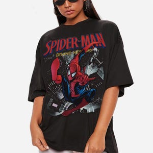 May include: Black t-shirt with a Spider-Man graphic. The design features the words "SPIDER-MAN" in red and blue, and an image of Spider-Man in action against a city backdrop. The t-shirt has short sleeves.