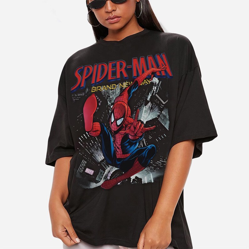 May include: Black t-shirt with a Spider-Man graphic. The design features the words "SPIDER-MAN" in red and blue, and an image of Spider-Man in action against a city backdrop. The t-shirt has short sleeves.