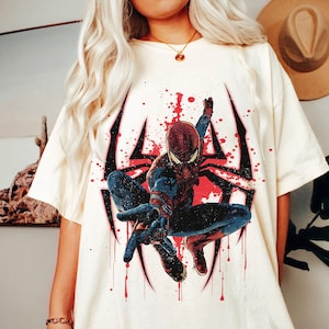 Puede incluir: Camiseta color crema con un gr&aacute;fico de Spider-Man en una pose din&aacute;mica. El dise&ntilde;o incluye un contorno de telara&ntilde;a negro con acentos rojos y efectos de salpicaduras. El superh&eacute;roe est&aacute; representado con su traje rojo y azul cl&aacute;sico.
