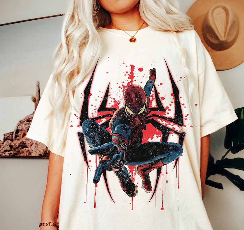 Puede incluir: Camiseta color crema con un gr&aacute;fico de Spider-Man en una pose din&aacute;mica. El dise&ntilde;o incluye un contorno de telara&ntilde;a negro con acentos rojos y efectos de salpicaduras. El superh&eacute;roe est&aacute; representado con su traje rojo y azul cl&aacute;sico.