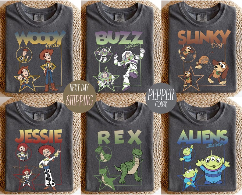 May include: Six charcoal gray t-shirts featuring characters from the animated film Toy Story. Each shirt displays a different character: Woody, Buzz, Slinky Dog, Jessie, Rex, and Aliens. The shirts have character names and images in various colors.