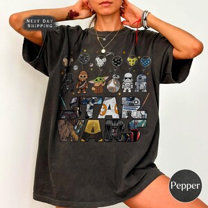 May include: Dark grey Star Wars t-shirt with a design of characters and the Star Wars logo. The shirt includes the text "NEXT DAY SHIPPING" in the upper left corner. The word "Pepper" is in a circle in the lower right corner.