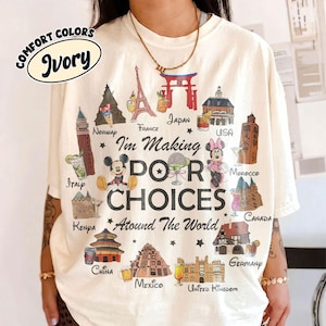 May include: An ivory t-shirt featuring a graphic print of global landmarks, cocktails, and cartoon characters. The text reads: I'm Making POOR CHOICES Around The World. The design includes illustrations of the Eiffel Tower, a torii gate, and various international buildings.