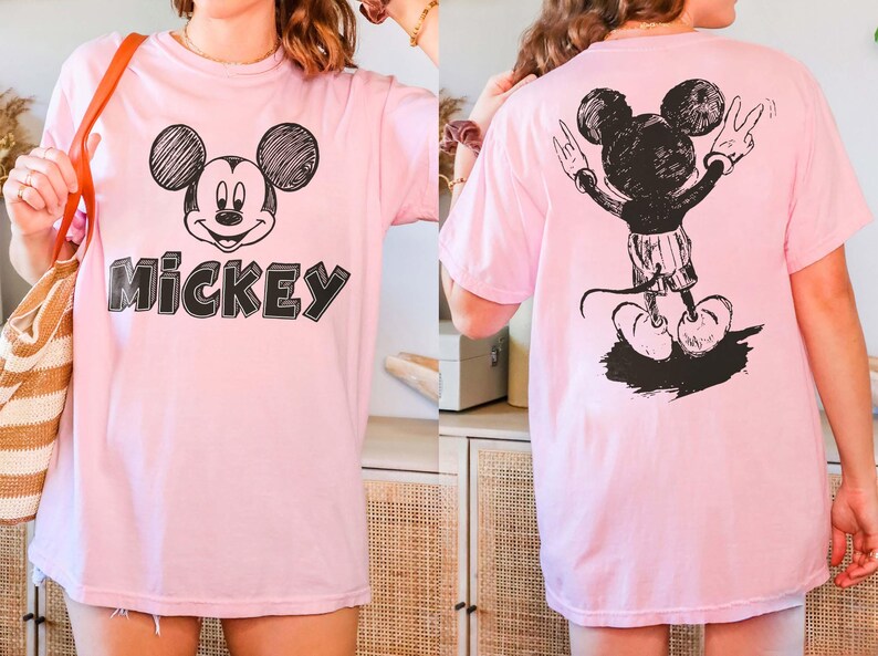 May include: Pale pink t-shirt with a black and white Mickey Mouse design on the front and back. The front graphic shows Mickey's face and the word "Mickey". The back graphic shows Mickey with his arms raised.