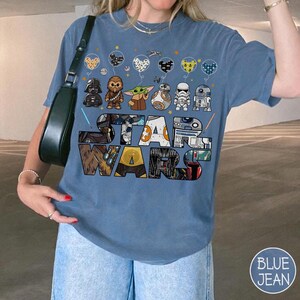 May include: A blue t-shirt with a Star Wars design, showcasing characters like Darth Vader, Chewbacca, Grogu, BB-8, a Stormtrooper, and R2-D2. The words 'STAR WARS' are prominently displayed. The design also includes balloon graphics. A casual, comfortable style.