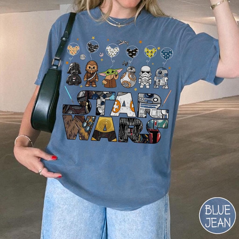May include: A blue t-shirt with a Star Wars design, showcasing characters like Darth Vader, Chewbacca, Grogu, BB-8, a Stormtrooper, and R2-D2. The words 'STAR WARS' are prominently displayed. The design also includes balloon graphics. A casual, comfortable style.