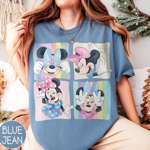 May include: Blue jean colored t-shirt featuring four panels with Minnie Mouse illustrations. Each panel showcases Minnie in different poses, wearing bows and dresses in pastel colors. The shirt has a relaxed fit.