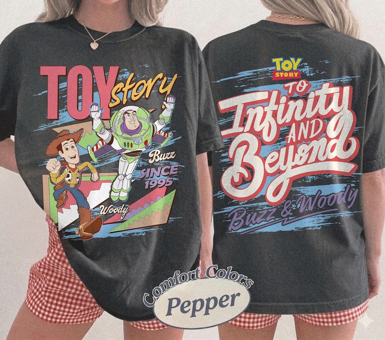 K&ouml;nnte beinhalten: Dunkelgraues T-Shirt mit dem Schriftzug "Toy Story" in Rot und einer Grafik von Woody und Buzz Lightyear. Auf der R&uuml;ckseite des Shirts steht der Schriftzug "To Infinity and Beyond" in Rot und Wei&szlig;. Das Shirt ist von der Marke Comfort Colors.