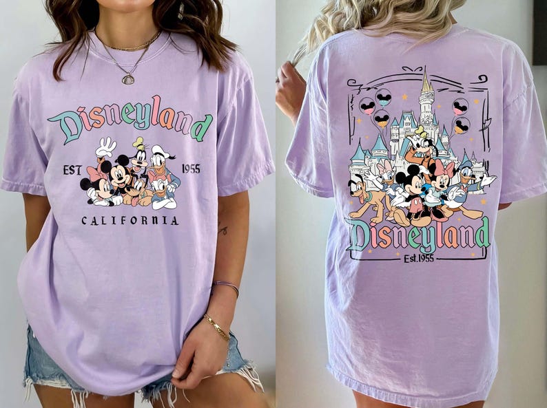 Może przedstawiać: Liliowa koszulka z logo Disneyland i grafiką Myszki Miki, Myszki Minnie, Kaczora Donalda i Goofy'ego. Prz&oacute;d koszulki przedstawia logo Disneyland i napis "EST 1955 CALIFORNIA". Tył koszulki ma grafikę zamku.