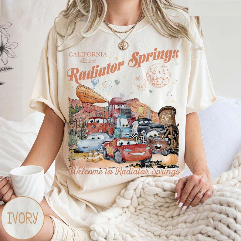 May include: A white ceramic mug with a black handle and the text "But First, Coffee" in a bold, black font. The mug is set against a blurred background, highlighting its clean design.