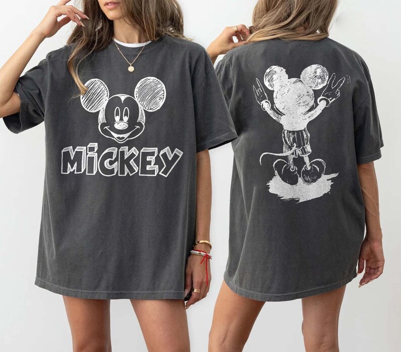 May include: Dark grey t-shirt with a white Mickey Mouse design on the front and back. The front displays Mickey's face and the word "Mickey". The back shows Mickey with his arms raised in a peace sign. A casual, unisex garment.