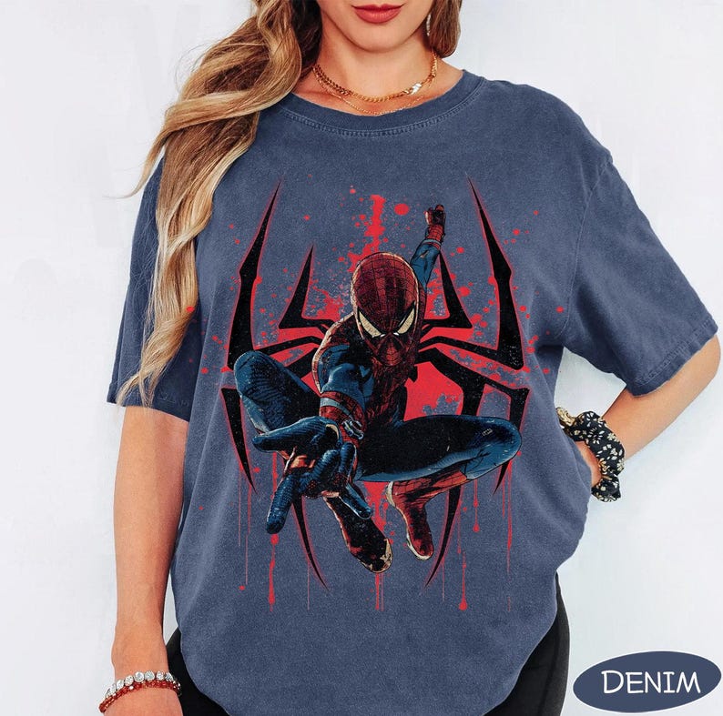 Puede incluir: Camiseta azul denim con un gr&aacute;fico de Spider-Man en una pose din&aacute;mica, sobre un dise&ntilde;o de telara&ntilde;a roja y negra. El superh&eacute;roe est&aacute; representado con su cl&aacute;sico traje rojo y azul. La palabra "DENIM" est&aacute; impresa en la parte inferior.