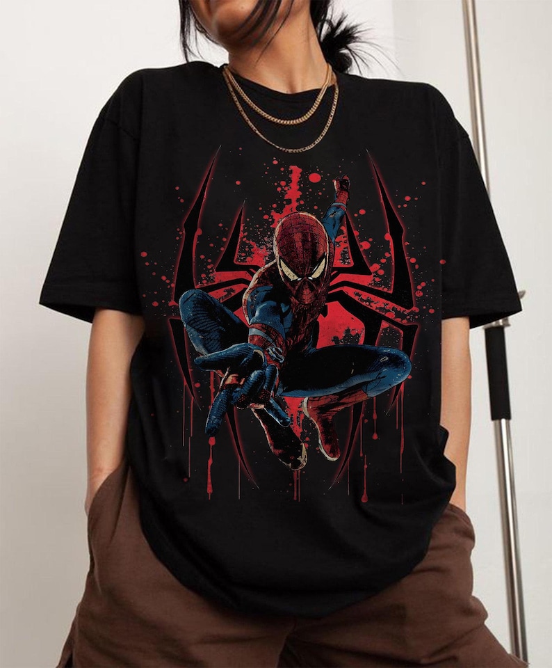 Puede incluir: Camiseta negra con un gr&aacute;fico de Spider-Man en una pose din&aacute;mica. El superh&eacute;roe est&aacute; representado con su cl&aacute;sico traje rojo y azul, sobre un dise&ntilde;o de telara&ntilde;a roja. El dise&ntilde;o incluye efectos de salpicaduras de pintura roja.