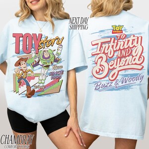 K&ouml;nnte beinhalten: Hellblaues T-Shirt mit Woody und Buzz Lightyear-Grafiken und dem Schriftzug "Toy Story". Auf der R&uuml;ckseite steht "To Infinity and Beyond" und "Buzz & Woody".