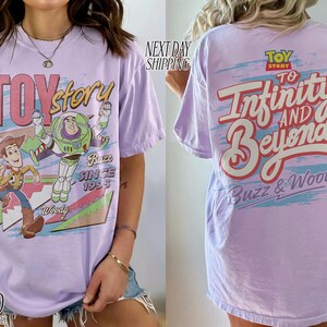 K&ouml;nnte beinhalten: Helllila T-Shirt mit den Toy Story-Charakteren Woody und Buzz Lightyear. Auf der Vorderseite stehen "Toy Story" und "Buzz Since 1995". Auf der R&uuml;ckseite steht "To Infinity and Beyond" und "Buzz & Woody".