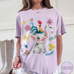 Pu&ograve; includere: T-shirt lilla con un design a fumetto di maiale e gallo, circondato da fiori e foglie. L'immagine &egrave; stampata su una maglietta a maniche corte, ideale per l'uso quotidiano.