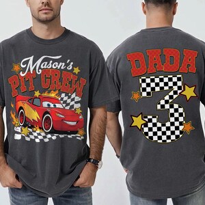 Peut inclure: T-shirt gris fonc&eacute; avec un dessin de voiture de course rouge et le texte "Mason's Pit Crew". Le dos du t-shirt affiche "DADA" et un num&eacute;ro 3 &agrave; damier avec des &eacute;toiles, parfait pour un anniversaire.