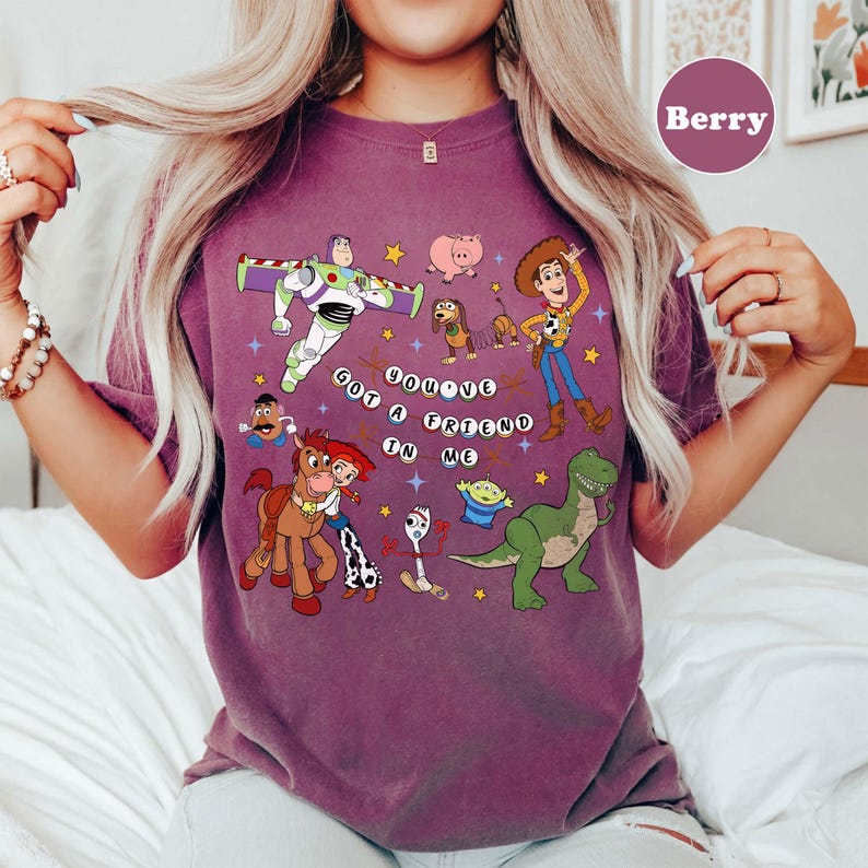 May include: Berry-coloured t-shirt with a graphic of characters from the animated film Toy Story. The design includes Buzz Lightyear, Woody, Jessie, and other characters, along with the phrase "You've Got a Friend in Me."